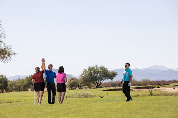 Four golfers celebrate a swing on a golf course in Salt River, Arizona.